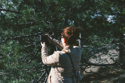 Rear view of woman photographing with smart phone by tree