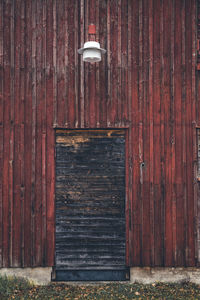 Wooden door to an abandoned old barn. up top is a lamp. with wild growing weeds. 