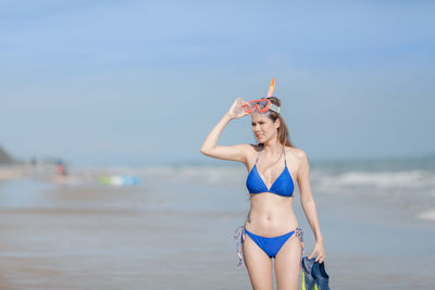 Beautiful woman looking away while standing on beach against sky