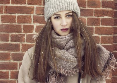 Portrait of young woman standing against brick wall