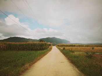 Road amidst field against sky