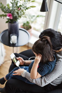 High angle view of mother and daughter wearing headphones while using mobile phone in living room