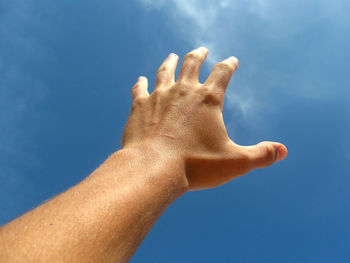 Cropped hand gesturing against blue sky