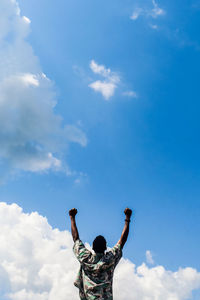 Low angle view of man with arms raised against sky