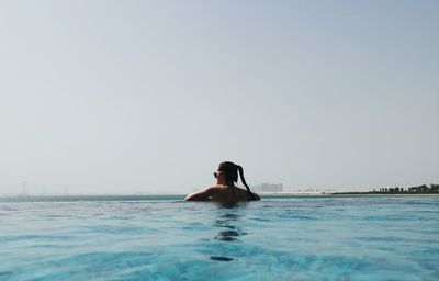 Rear view of young woman swimming in pool against clear sky