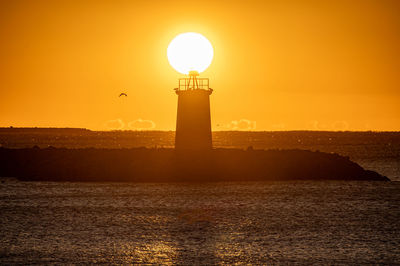 Lighthouse by sea against sky during sunset