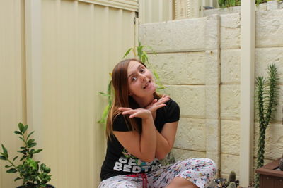 Portrait of cheerful woman making face against surrounding wall in back yard