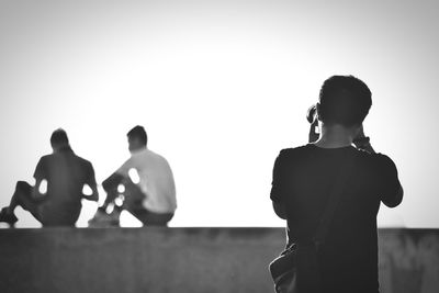 Rear view of man photographing people against clear sky