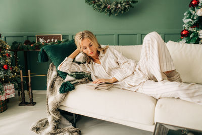 Attractive blonde woman in pajamas lying on a comfortable sofa in the living room reading a book
