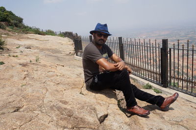 Full length portrait of young man sitting on land against sky