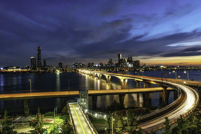 Illuminated bridge over river in city against sky at night