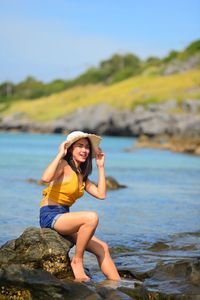Portrait of young woman sitting on rock by sea