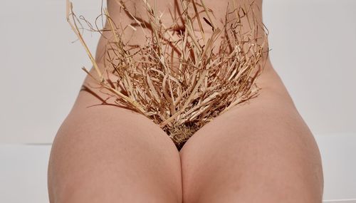 Midsection of woman with straw on vagina against white background