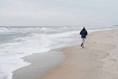 Rear view of woman walking at beach against sky