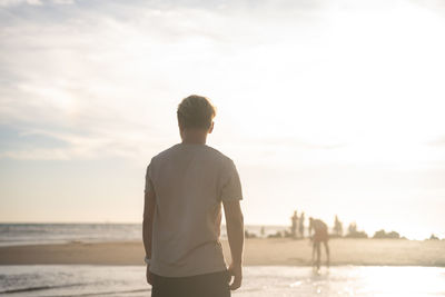 Rear view of man standing at beach against sky