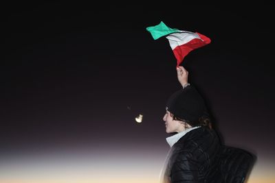 Side view of woman holding tricolor flag against clear sky at night