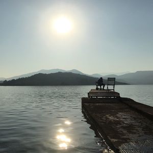 People sitting on lake against sky during sunset