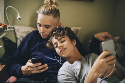 Teenage friends using mobile phone while leaning on bed at home