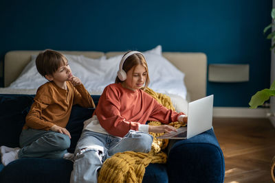 Children teen girl in headphones and boy study online class on laptop sitting on couch at home.