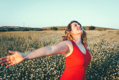 Beautiful young woman standing on field against clear sky