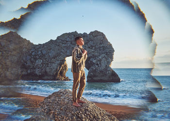 Digital composite image of young man standing on rock at beach