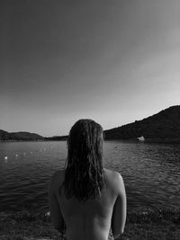 Rear view of shirtless woman at lakeshore against clear sky