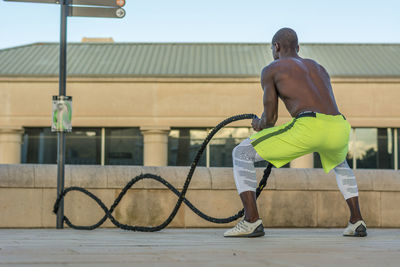 Full length of male athlete exercising with ropes