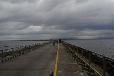 Jetty leading to sea against cloudy sky