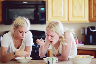 Sisters eating breakfast on table in kitchen