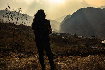 Young girl watching the misty mountain valley with sun rays beams at morning from flat angle