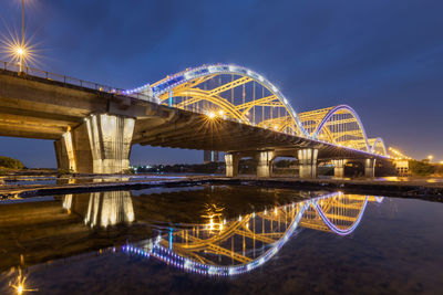 Illuminated bridge over river against sky at night