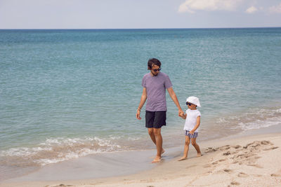 Man with a beard with a boy son walking on the beach by the sea in summer