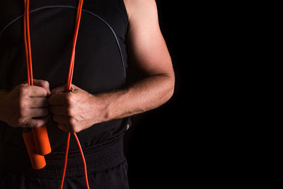 Midsection of man with jump rope against black background