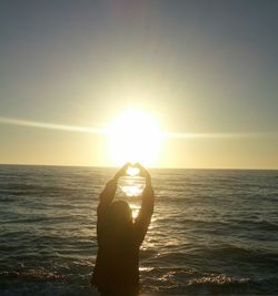 Silhouette person standing in sea against sky during sunset