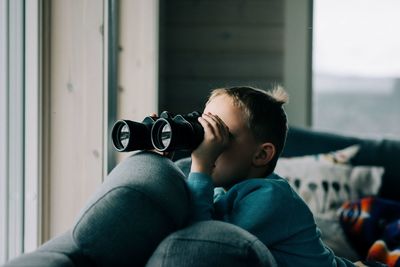 Young boy looking through binoculars at nature from a cosy cabin