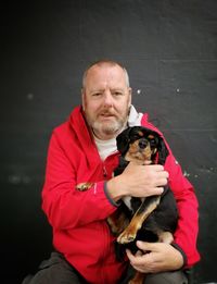 Portrait of mature man holding dog while sitting against wall