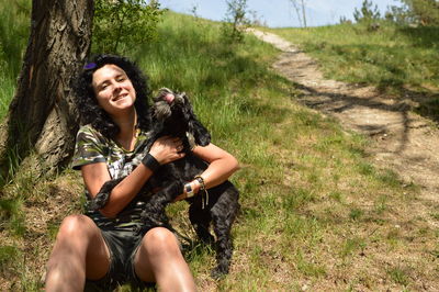 Portrait of woman with dog sitting on field against tree