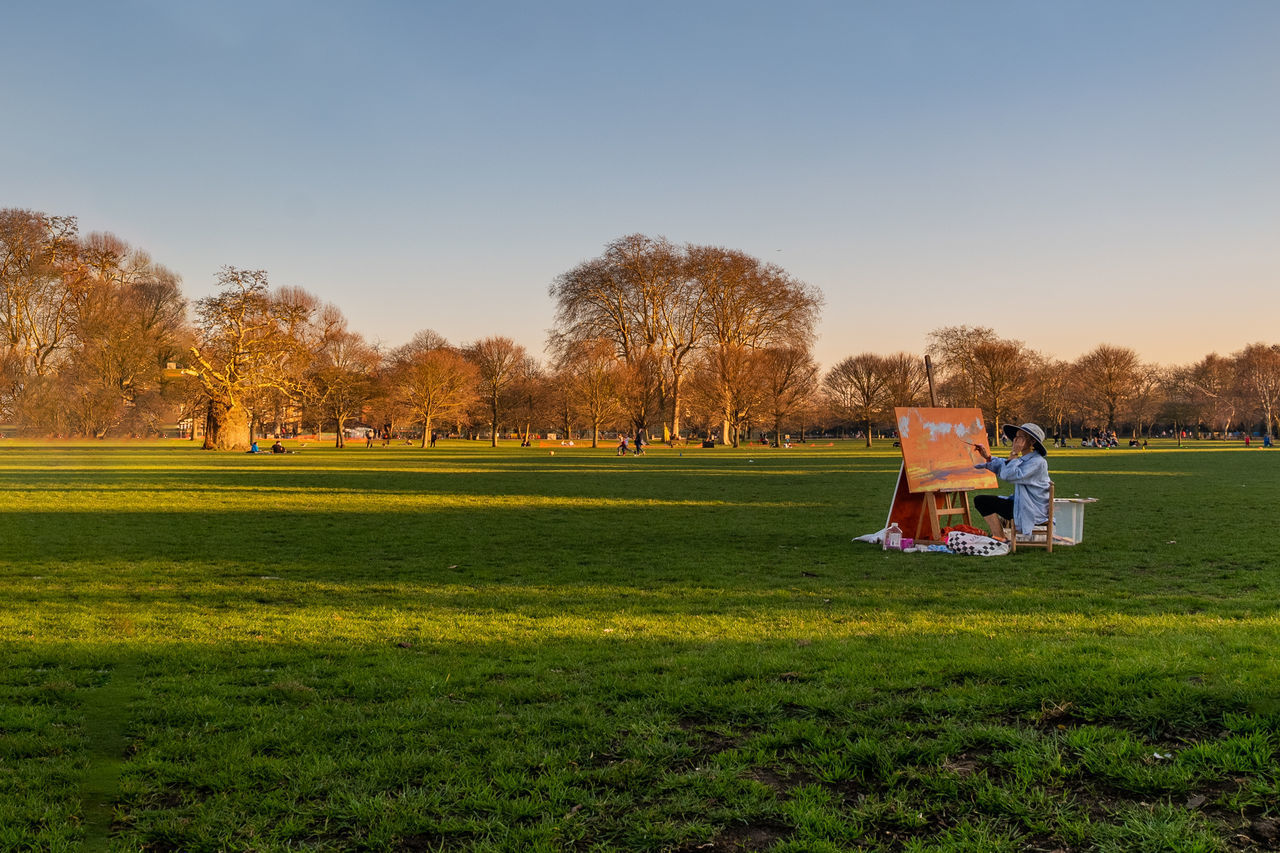 PEOPLE RELAXING ON FIELD AGAINST TREES