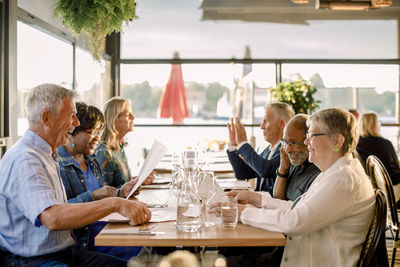 Happy senior men and women talking with each other while sitting together at table in restaurant