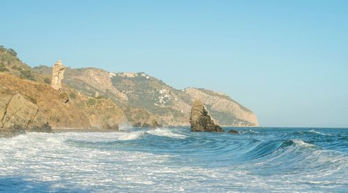 Rock formation in sea against clear blue sky