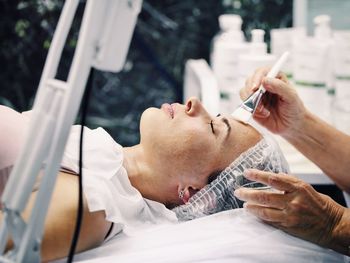 Cropped hands on cosmetologist applying cream on female customer head