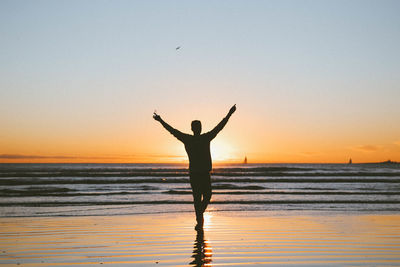 Silhouette of woman standing on beach at sunset