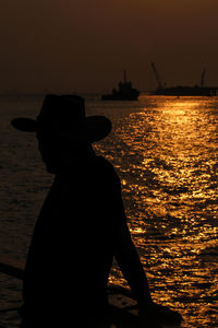 Silhouette man standing by sea against sky during sunset