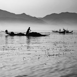 People fishing on shore by sea against sky