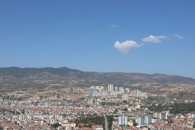 Aerial view of townscape and mountains against blue sky