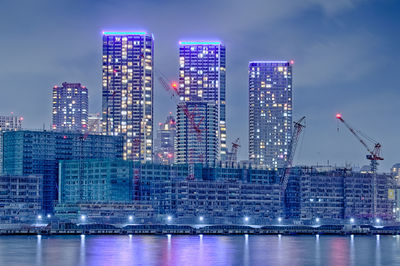 Illuminated modern buildings in city against sky at night