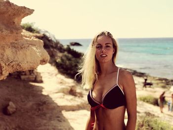 Portrait of beautiful young woman wearing bikini while standing against sea at beach