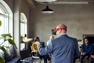 Rear view of mature businessman wearing vr gesturing at creative office