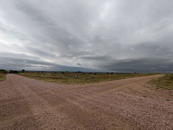 Dirt road amidst field against sky