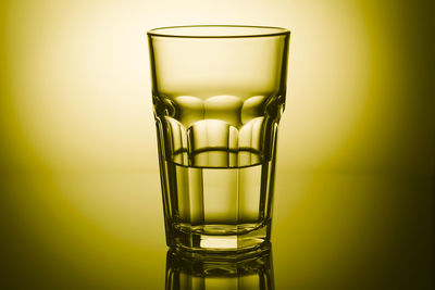 Half-filled highball glass in yellow light with mirror reflection. close-up